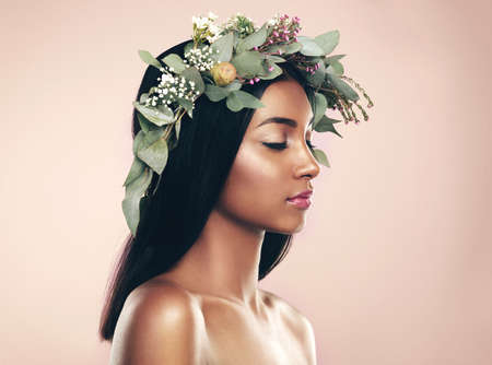 Revelling in natural beauty. Studio shot of a beautiful young woman wearing a wreath while posing with her eyes closed against a pink background.の写真素材