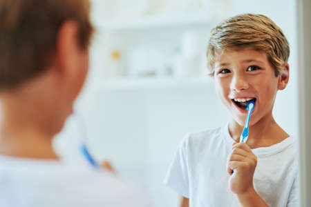 Keeping my teeth strong. Shot of a cheerful young boy looking at his reflection in a mirror while...