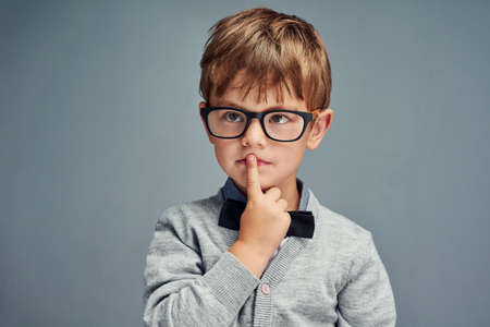 Question everything. Studio shot of a smartly dressed little boy looking thoughtful against a gray background.の写真素材