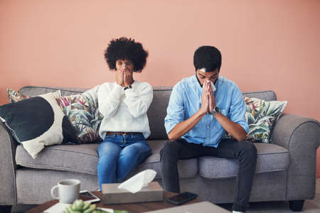 A few days later he got sick too. Shot of a young couple blowing their noses while sitting on the...