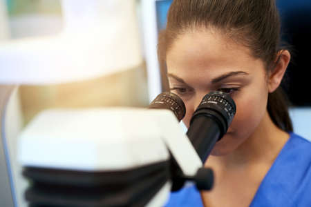 When working with microscopes, focus is key. Shot of a young pathologist looking at samples under a...