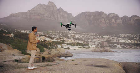 Soaring through the sky. Full length shot of a young man flying his drone outdoors.