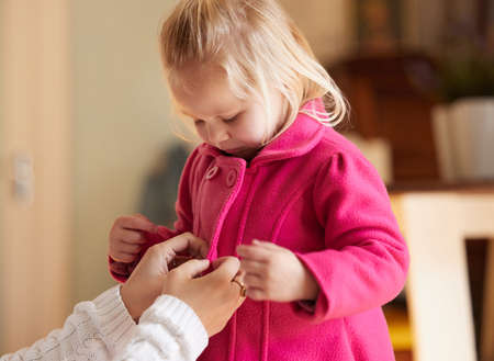 We have to stock up on cookies and milk. Shot of a woman buttoning up her daughters pink coat.の写真素材