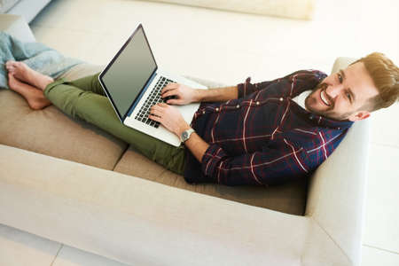 All I need for a lazy day at home. Shot of a relaxed young man using a laptop on the sofa at home.