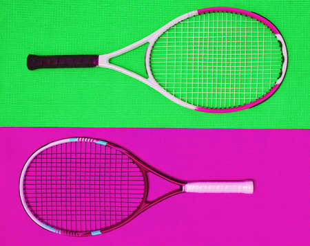 They are polar opposites. High angle shot of two tennis rackets placed together on top of a colourful background inside of a studio.の写真素材