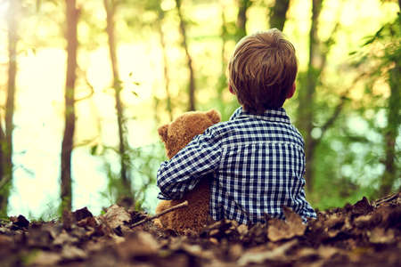Teddy is always by my side. Shot of a little boy sitting in the forest with his teddy bear.
