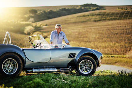Where to next. Shot of a senior man looking at a map while out on a roadtrip in a convertible.の写真素材