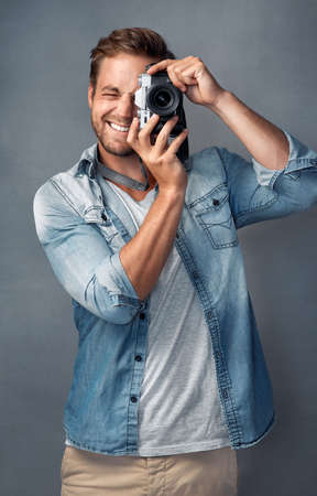 Put your happy face on. Portrait of a happy young man holding up a camera while posing against a gray background in the studio.の写真素材