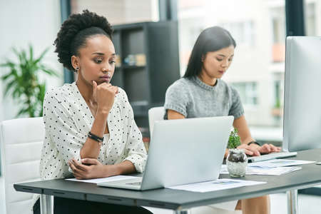 Focused on their work. Cropped shot of two young businesswomen working at their desk in the office.の写真素材