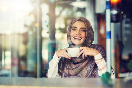Coffee is my afternoon delight. Portrait of a young woman having a cup of coffee in a cafe.の写真素材