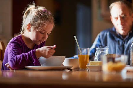 Grandpas keeping an eye on breakfast time. Cropped shot of a young girl eating cereal at the table with her grandfather in the background.