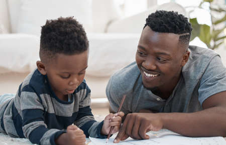 What about colouring this one. Shot of a young father lying on the the living room floor and helping his son draw.の写真素材