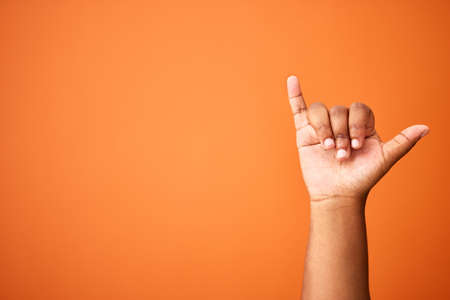 Lifes great. Shot of an unrecognizable person showing a shaka sign against an orange background.