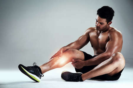 Nursing a calf injury. Full length shot of a sporty young man nursing a calf injury against a grey...
