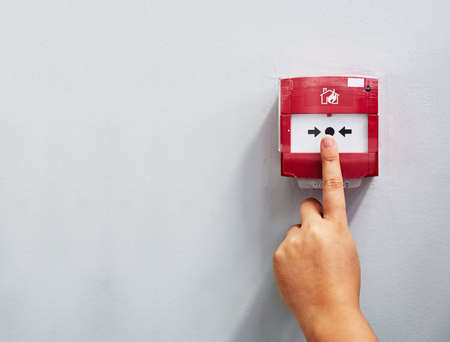 Activating the alarm. Cropped shot of a person pressing a fire alarm on a wall.