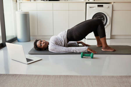 Becoming fit all in the privacy of her home. Shot of a young woman using a laptop while exercising...
