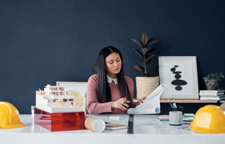 Shes fully dedicated to her job. Shot of an attractive young female architect going over paperwork...