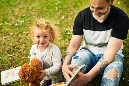 Giving her imagination infinite space to travel through reading. Shot of a father reading a story for his little daughter outdoors.の写真素材