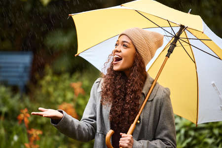 Making the best of a cold winters day. Shot of a young woman standing in the rain with an umbrella.の写真素材