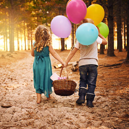 Best friends stick together. Shot of an unrecognizable little boy and girl holding a basket and balloons while walking outside in the woods.の写真素材