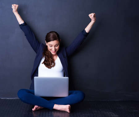 Business couldnt be better. Shot of a happy businesswoman looking at her laptop while raising her...