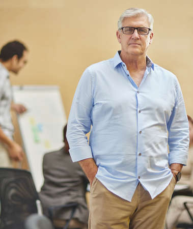I trust my team. Cropped portrait of a handsome mature man standing with his hands in his pockets in the boardroom with his colleagues in the background.の写真素材