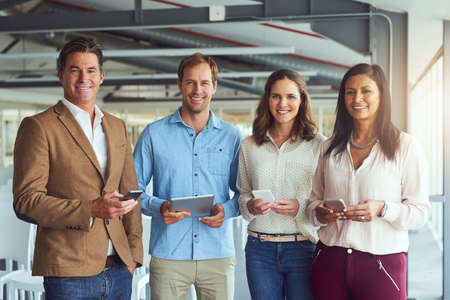 They believe in a strong online presence. Portrait of a team of businesspeople posing with their wireless devices in the office.の写真素材
