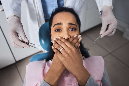 Its business as usual until they bring the tools out. Shot of a young woman looking scared while having dental work done on her teeth.の写真素材