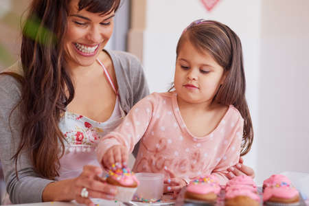 Adding some sprinkles to top it all off. Cropped shot of a little girl baking together with her mother at home.の写真素材