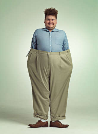 Diet progress. Shot of an overweight man wearing a pair of oversized pants looking pleased.の写真素材