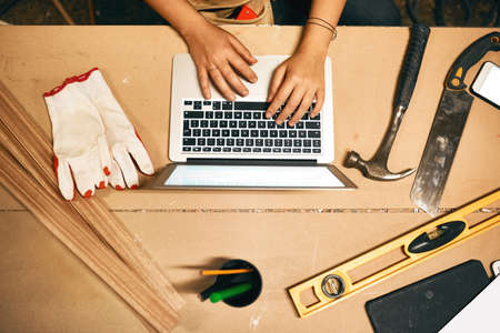 Going back to some research. High angle shot of an unrecognizable carpenter working on a laptop...