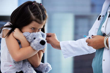 Id rather be at the park. Shot of a scared little girl getting a vaccination in a hospital.の写真素材