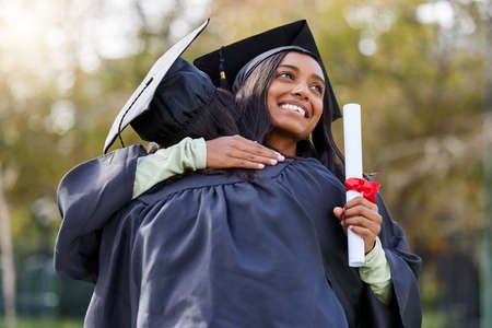 We did it. Cropped shot of an attractive young female student hugging her friend while celebrating on graduation day.の写真素材