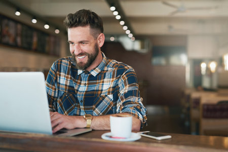 Coffee and cat videos - a classic combination. Shot of a young man using his laptop while sitting by the window in a cafe.