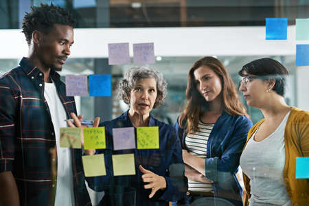 Great concepts in the making. Shot of a group of colleagues working with adhesive notes on a glass...