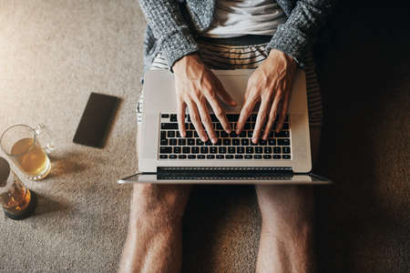 Uncapped wifi means limitless browsing. High angle shot of an unrecognizable man using his laptop while sitting on the floor at home at home.の写真素材