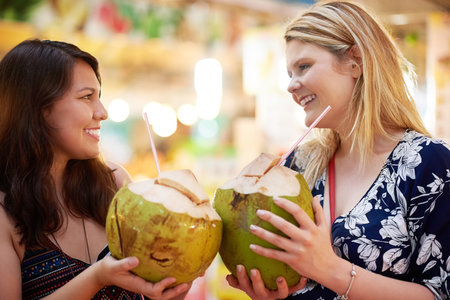 Together on three. Cropped shot of two young women drinking from coconuts in a foreign grocery store.の写真素材