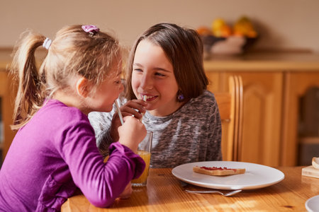 Smiles at the breakfast table. Cropped shot of a smiling little girl having breakfast with her sister in the kitchen.の写真素材