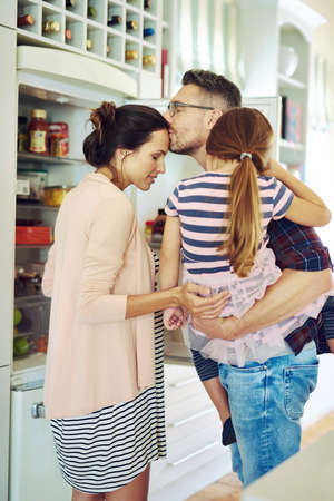 Bound together by love. Shot of a husband lovingly kissing his wife in the kitchen with his family.の写真素材