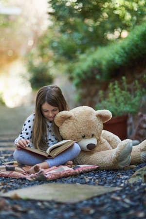 Teddy seems to be taking a nap from storytime. Shot of a little girl reading a book with her teddy...