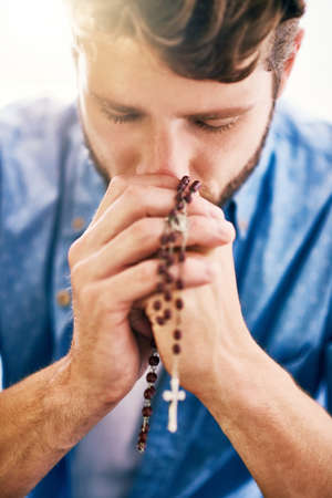 Putting his faith first. Cropped shot of a young man holding his rosary while praying.の写真素材