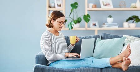 Caffeines always there to help you chill. Full length of a young woman using her laptop while having...