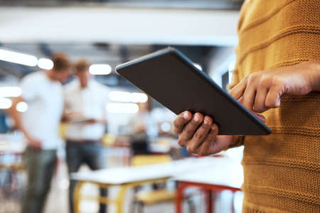 Modern technology for modern success. Cropped shot of an unrecognizable young businesswoman in the office with his colleagues in the background.の写真素材