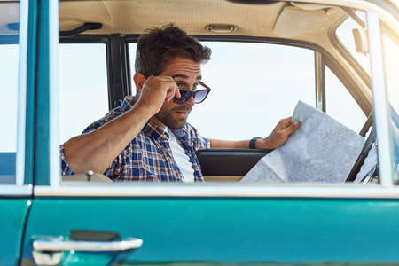 Am I on the right track. Cropped shot of a handsome man checking a map while enjoying a roadtrip.の写真素材
