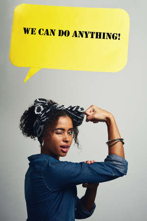 There is strength in being a woman. Studio shot of an attractive young woman posing with a speech bubble that reads We can do anything against a grey background.の写真素材