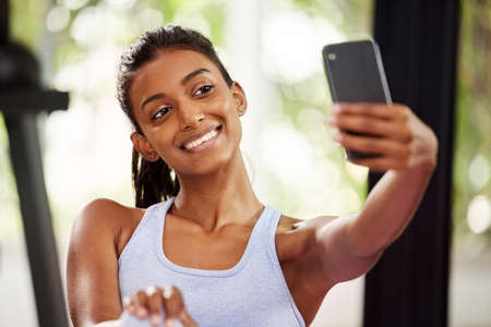 Nothing makes me feel happier than a finished workout. Shot of a beautiful young woman taking a selfie while at the gym.の写真素材