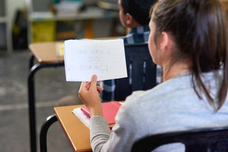 Tell me something I dont know. Rearview shot of an unidentifiable schoolgirl reading a note in...