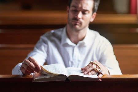 Hearing Gods voice through his verse. Shot of a young man reading the bible in church.の写真素材