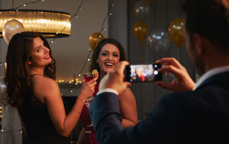Capturing the moment. Cropped shot of an unrecognizable man taking a photograph of two attractive young women in a nightclub.の写真素材