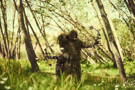 Its all about aim. Shot of a father and son in camouflage hunting with bows and arrows in the woods.